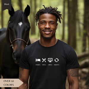 Puede incluir: Una camiseta negra con un diseño gráfico blanco que presenta iconos para dormir, comer, codificar y un símbolo de actualización. El texto debajo de los iconos dice "sleep(); eat(); code(); repeat();".