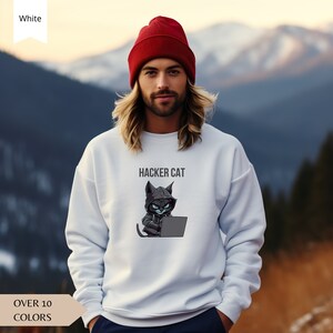 Può includere: Felpa bianca con un gatto nero che indossa una felpa con cappuccio e tiene un laptop. Il testo "HACKER CAT" è stampato sopra il gatto.