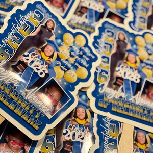 May include: A collection of graduation stickers featuring a graduate in a cap and gown. The stickers are blue and white with the text "Congratulations Class of 2026" and the graduate's name and university. There are also photos of the graduate.