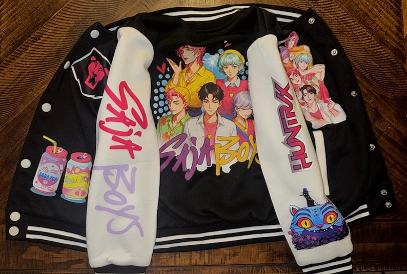 Puede incluir: Una chaqueta universitaria negra y blanca con un estampado gr&aacute;fico de cinco personajes estilo anime en la espalda. Las mangas son blancas con texto rosa y morado que dice Saja Boys y Huntrax, junto a ilustraciones de latas y un gato.