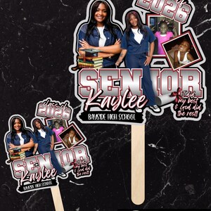May include: Two graduation photo props featuring a young woman, the text "SENIOR Kaylee", and "Class of 2026". One prop includes the text "Bayside High School" and "I did my best & God did the rest!". The props are on wooden sticks.
