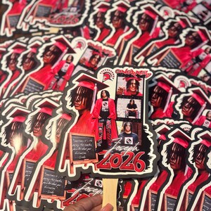 May include: A collection of graduation fan favors featuring a young person in a red graduation gown and cap. The fans have a black border and include the name "Joseph" and the year "2026" in red. The fans also have the word "CONGRATS" and a quote.