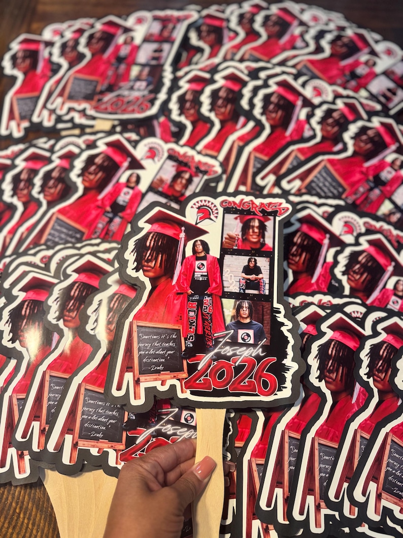 May include: A collection of graduation fan favors featuring a young person in a red graduation gown and cap. The fans have a black border and include the name "Joseph" and the year "2026" in red. The fans also have the word "CONGRATS" and a quote.