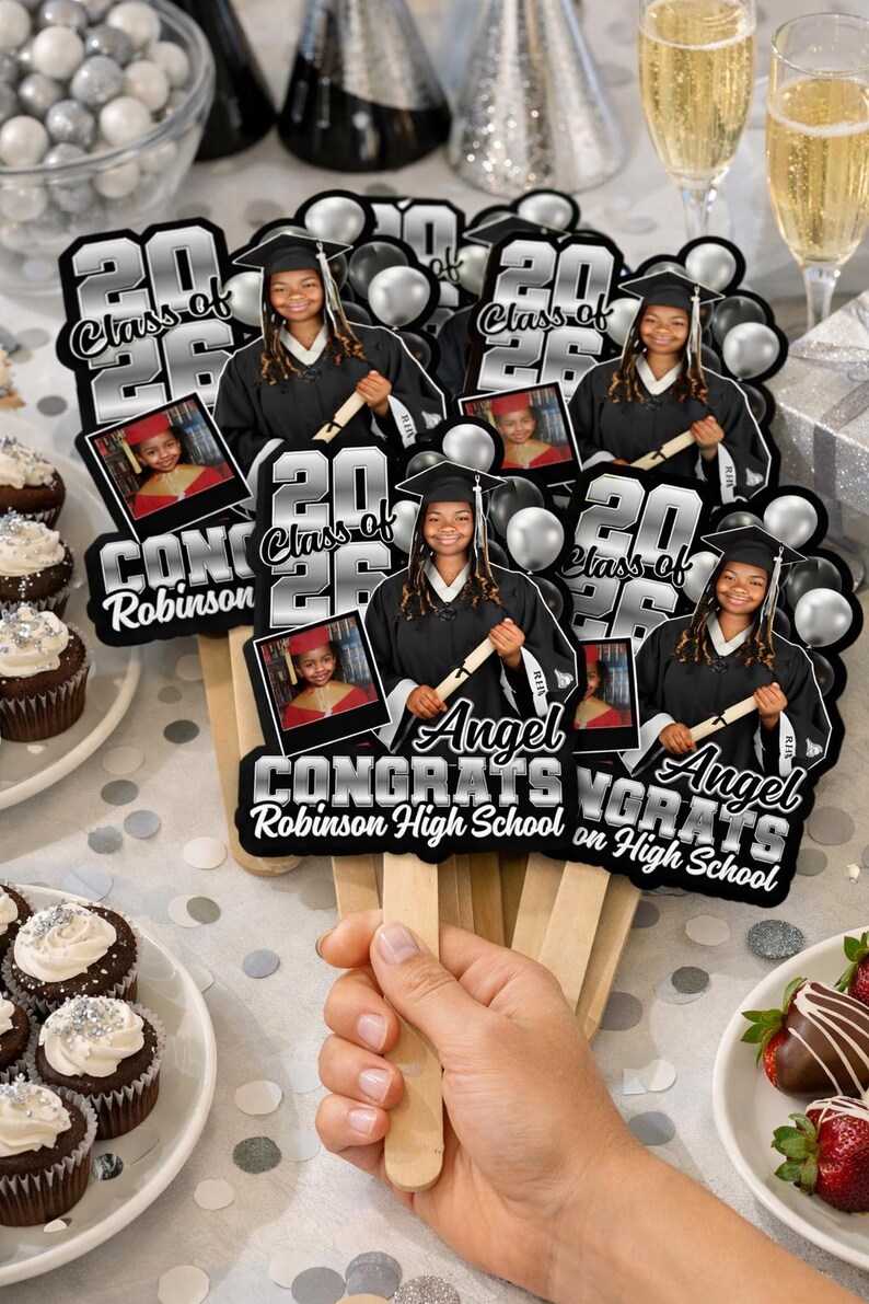 May include: A hand holding graduation fans with the text "Class of 2026" and "Congrats Angel Robinson High School on High School". Each fan features a photo of a graduate in a cap and gown, with black and silver accents.