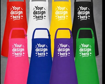 Puede incluir: Una colección de ocho delantales en rojo, blanco, amarillo, negro, rosa, azul, morado y verde. Cada delantal cuenta con una correa ajustable para el cuello y el texto impreso "Your design here" con pequeños iconos de corazones.