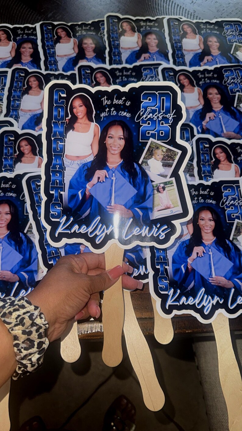 May include: A collection of graduation fans featuring a young woman in a blue graduation gown. The fans have the text "Congrats" and "Class of 2025" with the name "Kaelyn Lewis". The fans are held together with wooden sticks.
