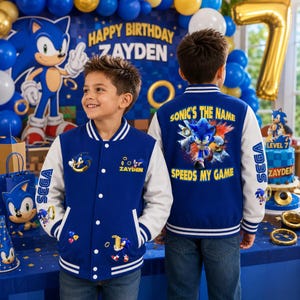 Puede incluir: Una chaqueta universitaria azul y blanca con gr&aacute;ficos de Sonic the Hedgehog. El frente muestra el nombre Zayden, mientras que la espalda presenta el texto Sonic's the name, speeds my game. Las mangas tienen la marca Sega y estampados de Sonic.