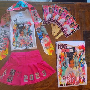 May include: A graduation set featuring a white t-shirt, pink pleated skirt, sash, and fans. The set includes the name "Taryn" and "Pre-K Graduate" with the year "2025". The items are decorated with colorful graphics.