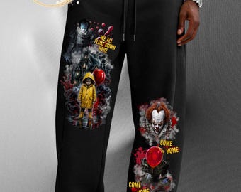 Puede incluir: Pantalones de chándal negros con estampados gráficos de un payaso y un niño con impermeable amarillo. La pierna izquierda muestra el texto "WE ALL FLOAT DOWN HERE" con una casa y un globo rojo. La pierna derecha presenta un payaso y "COME HOME".