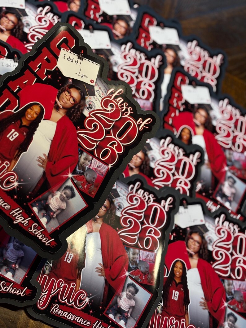 May include: A stack of graduation announcements with a black border. The announcements feature a photo of a graduate in a red graduation gown, the text "Class of 2026", and the graduate's name. A small note says "I did it!"
