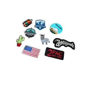 May include: A collection of embroidered patches including a cactus, a US flag, a donkey, a mountain shield, a circular mountain badge, a backpack, a round mountain scene, a Whitesnake logo, and a black rectangular 2PAC 1971-1996 patch.