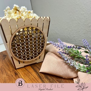Puede incluir: Una caja de palomitas de maíz de madera con un diseño de celosía decorativo. La caja está llena de palomitas de maíz y está sobre una superficie de madera.