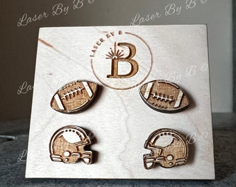 May include: Four wooden laser cut football themed earrings on a wooden display stand. The earrings are a football, a football helmet, and two footballs. The stand has the words "Laser By B" on it.