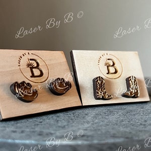 May include: Two sets of wooden earrings displayed on cards. The first set features a cowboy boot design, the second set features a cowboy hat design. The cards have the text "Laser By B" printed on them.