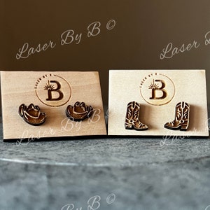 May include: Two pairs of wooden earrings displayed on a wooden card. The first pair features a cowboy hat and the second pair features a cowboy boot.