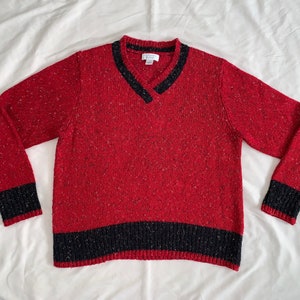 May include: Red and black knit sweater with a v-neck and a black band around the bottom.