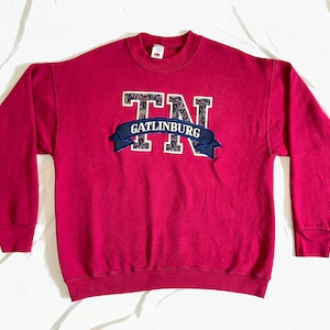 May include: A maroon sweatshirt with a large embroidered patch that says "TN Gatlinburg" in white and blue lettering.