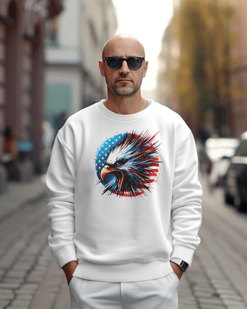 May include: White sweatshirt with a graphic of an eagle's head in front of an American flag. The eagle is red, white, and blue with a black beak and eyes.