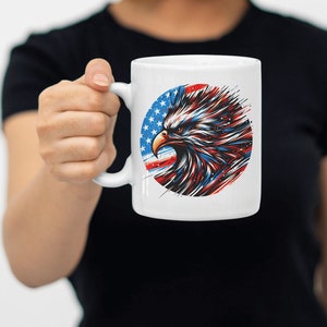 May include: White ceramic mug with a graphic of an eagle's head in front of an American flag. The eagle's head is red, white, and blue.