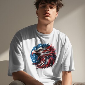 May include: White t-shirt with a graphic of an eagle's head with red, white, and blue feathers. The eagle is in front of a circle of stars.