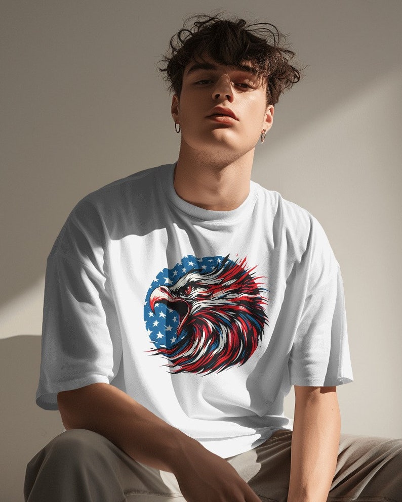 May include: White t-shirt with a graphic of an eagle's head with red, white, and blue feathers. The eagle is in front of a circle of stars.