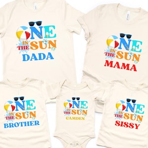 Puede incluir: Un conjunto de cinco camisetas y un body de color crema con un estampado gr&aacute;fico que dice ONE IN THE SUN junto a una pelota de playa, gafas de sol y un helado. Las prendas incluyen las palabras DADA, MAMA, BROTHER, SISSY y CAMDEN.