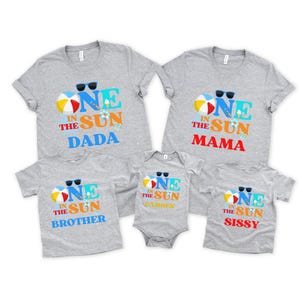 Puede incluir: Un conjunto de cinco camisetas y un body de color gris jaspeado con un gr&aacute;fico de tem&aacute;tica playera y el texto ONE IN THE SUN. Cada prenda incluye ilustraciones de una pelota de playa, gafas de sol y helado, con las etiquetas DADA, MAMA, BROTHER, SISSY y CAMDEN.