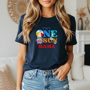 Puede incluir: Una camiseta azul marino de manga corta con un estampado gr&aacute;fico colorido que dice ONE IN THE SUN MAMA. El dise&ntilde;o incluye una pelota de playa, gafas de sol, un helado, un flotador y chanclas en tonos brillantes de azul, amarillo y rojo.
