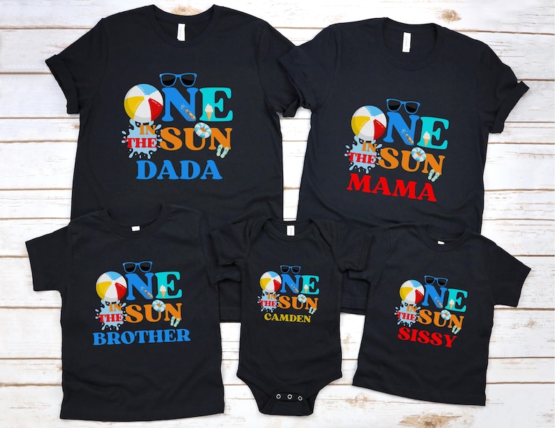 Puede incluir: Un conjunto de cinco camisetas negras y un body negro con un estampado gr&aacute;fico con el texto ONE IN THE SUN. El dise&ntilde;o incluye una pelota de playa, gafas de sol e iconos de helados. Las camisetas est&aacute;n etiquetadas como DADA, MAMA, BROTHER, CAMDEN y SISSY.