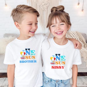 Puede incluir: Dos camisetas blancas de manga corta con un estampado gr&aacute;fico colorido. El dise&ntilde;o incluye una pelota de playa, gafas de sol y el texto ONE IN THE SUN BROTHER en una camiseta y ONE IN THE SUN SISSY en la otra, con salpicaduras de agua azul.