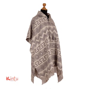 May include: A hooded alpaca wool poncho with a geometric pattern in shades of gray and white. The poncho has a zipper closure and fringe trim.