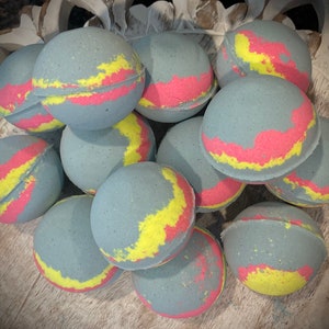 May include: A group of bath bombs in various shades of blue, yellow, and pink. The bath bombs are round and have a swirl pattern.
