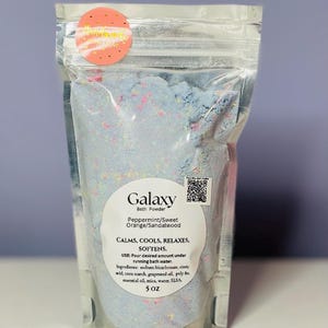 May include: A clear plastic pouch with a zipper closure containing a blue, pink, and white bath powder. The label reads "Galaxy Bath Powder Peppermint/Sweet Orange/Sandalwood CALMS, COOLS, RELAXES, SOFTENS. USE: Pour desired amount under running bath water. Ingredients: sodium bicarbonate, citric acid, corn starch, grapeseed oil, poly 80, essential oil, mica, water, SLSA. 5 oz"