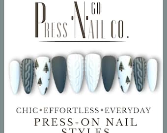 May include: A collection of press-on nails in various designs. The nails feature matte gray, white cable knit, and white nails with small Christmas tree designs. The text "PRESS N GO NAIL CO." is at the top, with "CHIC • EFFORTLESS • EVERYDAY PRESS-ON NAIL STYLES" below.