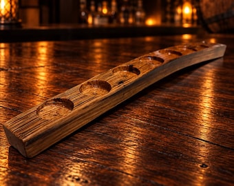 May include: A curved wooden flight board featuring five circular indentations for holding glasses. The board is crafted from dark, textured wood with a visible grain pattern, showcasing a long, narrow shape designed for serving multiple beverages.