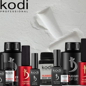 Pode incluir: Uma variedade de produtos para unhas KODI PROFESSIONAL, incluindo Rubber Base Gel e Rubber Top Gel, em frascos pretos com rótulos brancos e vermelhos. A marca está no topo. Fundo branco texturizado.