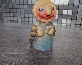 Könnte beinhalten: Eine Vintage-Gummi-Spielfigur mit einem skurrilen Design. Die Figur hat einen beigefarbenen Kopf mit blauen Augen, einen roten Mund und einen hellblauen und beigefarbenen Körper. Die Figur steht auf einer dunkelgrauen Oberfläche.