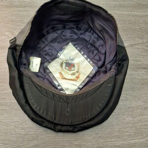 Może przedstawiać: Czarna i szara czapka Kangol, widziana od wewnątrz. Wnętrze posiada pikowaną granatową podszewkę i białą metkę z herbem. Czapka ma zakrzywiony daszek i strukturalny kształt.