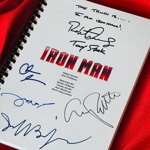 以下が含まれることがあります： 「アイアンマン」というタイトルが赤と黒の文字で書かれた白い脚本。脚本には、ロバート・ダウニー・ジュニア、トニー・スターク、ジョン・ファブロー、マーク・ファーガス、ホーク・オストビー、アート・マーカム、マット・ホロウェイの署名があります。テキストには「THE TRUTH IS..... I AM IRON MAN!」と書かれています。