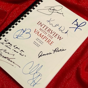 May include: A white book with the title "Interview with the Vampire" and the names of the director and writer, Neil Jordan and Anne Rice. The book is signed by five people, including Anne Rice.