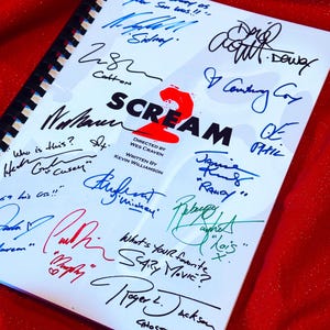 Könnte beinhalten: Ein spiralgebundenes Drehbuch für den Film "Scream 2" mit zahlreichen Unterschriften in verschiedenen Farben. Der Titel "SCREAM 2" ist prominent dargestellt, darunter die Namen des Regisseurs und des Drehbuchautors. Der Hintergrund ist eine strukturierte rote Oberfläche.