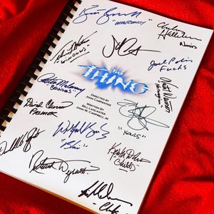 May include: A white spiral-bound script featuring numerous signatures in blue and black ink. The title "THE THING" is displayed in blue, set against a red backdrop. The script also includes the director's and writers' names.
