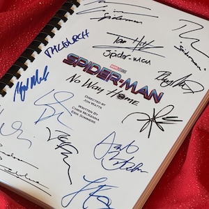 Può includere: Un libro di sceneggiatura bianco con un logo Spider-Man rosso e blu e il titolo "No Way Home". Il libro è firmato da diverse persone, tra cui Tom Holland, Zendaya, Jacob Batalon e altri. Il libro è su una superficie rossa.