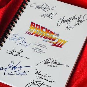 May include: A white notebook with the Back to the Future III logo and signatures from the cast, including Michael J. Fox, Christopher Lloyd, Lea Thompson, Thomas F. Wilson, and others.