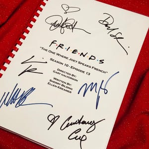 Pode incluir: Um roteiro da série de TV "Friends" com várias assinaturas em tinta preta e azul. O roteiro é intitulado "The One Where Joey Speaks French" e é da 10ª temporada, episódio 13. O roteiro está em papel branco com encadernação em espiral vermelha.