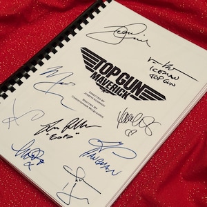 May include: A white script with the title "Top Gun Maverick" and the text "Directed by Joseph Kosinski" and "Written by Christopher McQuarrie". The script is signed by several people, including "Iceman Top Gun".