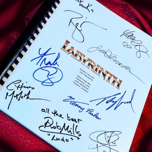 Puede incluir: Un guion blanco con el título "LABYRINTH" en letras doradas. El guion está firmado por varias personas, entre ellas Jim Henson, Terry Jones y Rob Mills. Las firmas están en tinta azul.
