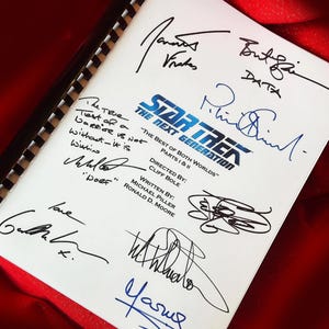 Puede incluir: Una página blanca con texto negro y varias firmas azules. El texto dice "Star Trek: La Nueva Generación" y "Lo mejor de ambos mundos" Partes I & II. Las firmas incluyen "Brent Spiner", "Data", "Patrick Stewart", "Gates McFadden", "Jonathan Frakes", "Michael Dorn", "Wil Wheaton" y "Yasuhiro Nakasone".