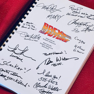 May include: A white notebook with the title "Back to the Future" and signatures from the cast and crew. The signatures include Marty McFly, Doc Brown, Biff Tannen, and Lorraine Baines.