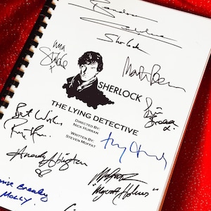 Puede incluir: Un cuaderno con espiral blanco con el título "THE LYING DETECTIVE" y una silueta de Sherlock Holmes. La portada está llena de firmas en tinta negra y azul, con la palabra "SHERLOCK" en un lugar destacado.